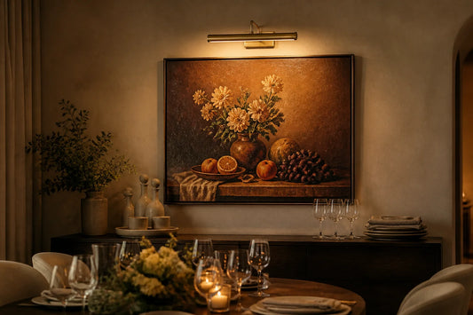 Antique brass wireless picture light mounted above framed still life oil painting in an intimate dining room setting